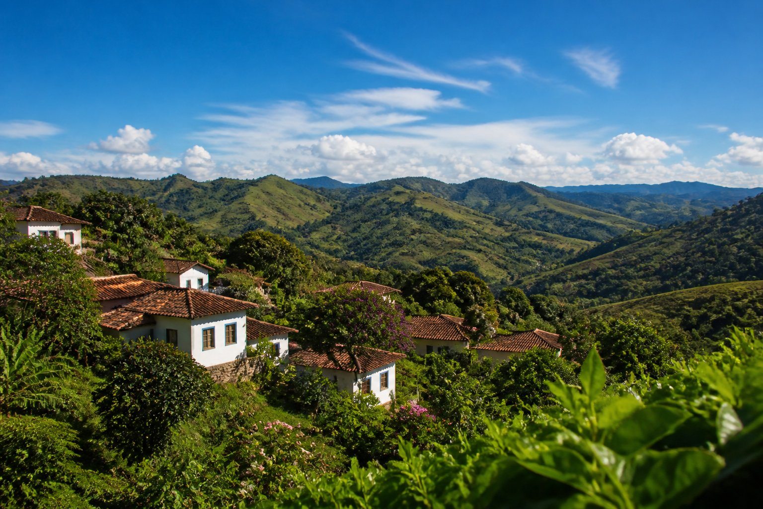 Vista panorâmica das colinas verdes de Serro, Minas Gerais, com casas coloniais e vegetação nativa sob céu azul.